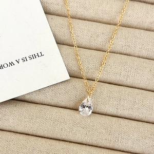 Macro shot of elegant gold teardrop zircon necklace displayed on beige velvet