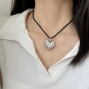 Collier élégant avec pendentif cœur argenté et cordon noir porté sur un polo blanc
