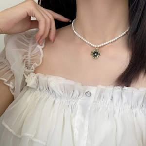 Elegant pearl necklace featuring a black clover pendant with gold trim on model