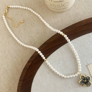 Detail of white pearl necklace with gold beads and a black clover pendant on wooden tray
