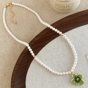 Detail of pearl necklace featuring a green clover pendant and gold-plated clasp on wood