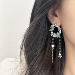 Elegant earrings with light blue gemstones, pearls, and gold tassels worn by a model
