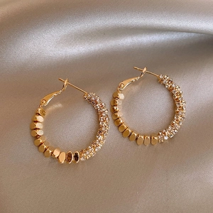 Detailed close-up of golden hoop earrings with pavé zircons on champagne silk fabric