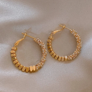 Detail of gold hoop earrings with sparkling rhinestones and textured oval metal plates
