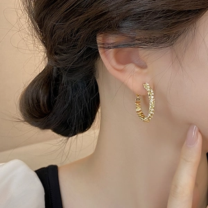 Detailed view of large gold hoop earrings with sparkling textured surface on model's ear