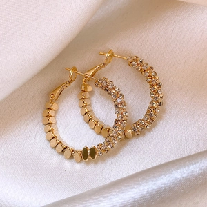 Detail of gold hoop earrings with sparkling rhinestones on elegant white silk background