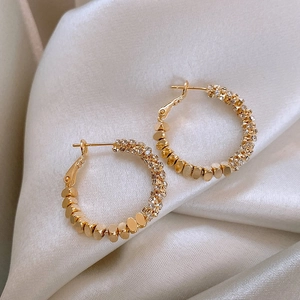 Detail of gold circular earrings featuring sparkling stones and metallic bead texture