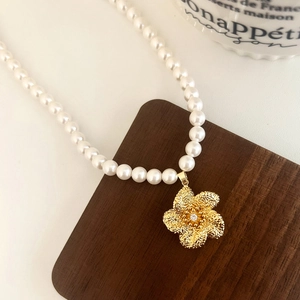 Élégant collier de perles avec pendentif fleur dorée et cristal sur présentoir en bois