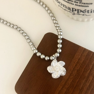Détail d'un collier de perles grises avec un pendentif floral argenté scintillant