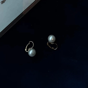 Elegant gold leverback pearl drop earrings with white pearls over a dark textured backdrop
