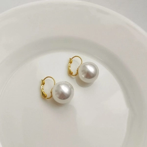 Elegant gold leverback earrings with round white pearls on a minimalist white ceramic plate