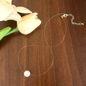 Detail of single pearl on invisible fishing line necklace with gold clasp on wood
