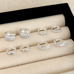 Détails de boucles d'oreilles argentées serties de zircons sur présentoir beige