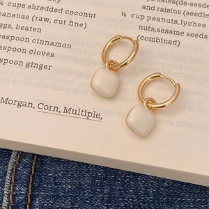 Elegant gold hoop earrings with white enamel square charms on a vintage book backdrop