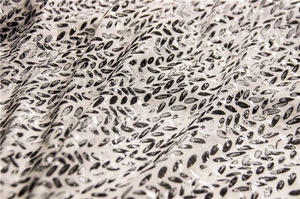 Detail of white cotton linen scarf featuring black leaf prints and shimmering sequins