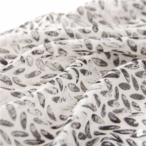 Macro shot of cotton linen scarf detail featuring black leaf prints and soft fabric drape