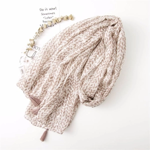 Detail of soft linen scarf featuring brown leaf patterns and elegant tassel edges