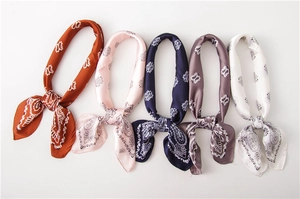 Flat lay of five paisley satin scarves in orange, navy, and pink on white background