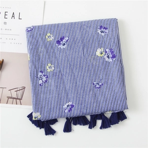 Detail of blue striped linen cotton scarf with floral print and fringe tassels on a table