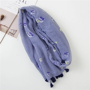 Detail of blue striped cotton scarf with floral print and dark blue fringe tassels