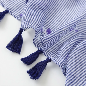 Detail of blue striped cotton scarf featuring purple floral print and navy blue tassels