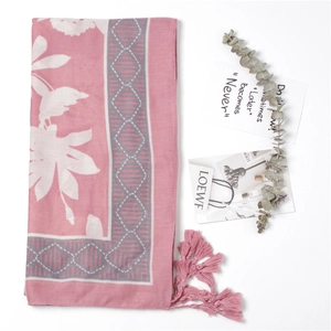 Flat lay of soft pink linen scarf with floral print, tassels and decorative botanicals