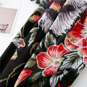 Dettaglio dello scialle in cotone e lino con fiori rossi e nappe nere decorative