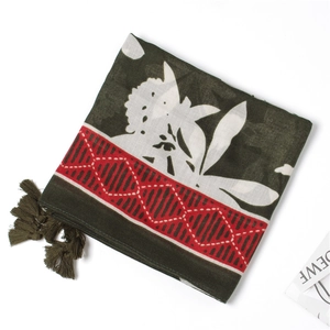 Detailed texture of olive green linen scarf featuring white floral patterns and red borders
