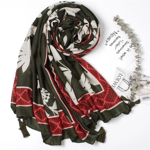 Close-up of green leaf print scarf with red geometric borders and tassel details