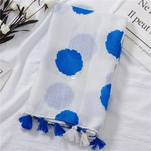 Detail of white cotton linen scarf featuring blue dots, silver accents, and tassel edges