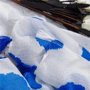 Close-up of white linen scarf with royal blue prints, silver sequins, and fringed tassels