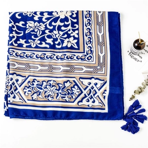 Détail d'une écharpe ethnique bleue et dorée à motifs floraux et pompons en soie