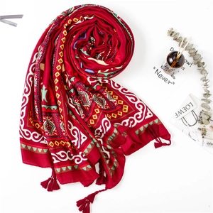Détail d'un châle à motif ethnique rouge avec pompons sur un fond blanc épuré
