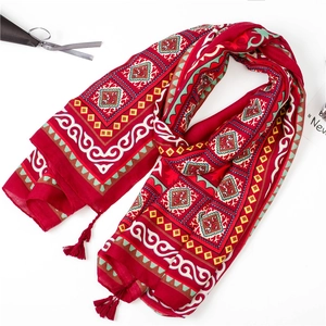 Gros plan d'une écharpe ethnique rouge à motifs géométriques et pompons sur fond blanc