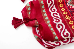Détail macro d'un châle ethnique rouge avec motifs géométriques et bordure à franges