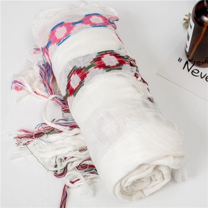Close-up of white cotton linen scarf with geometric embroidery and long tassel fringe
