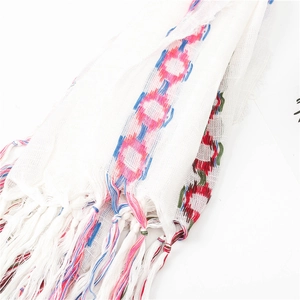 Detail of white cotton linen scarf featuring colorful embroidered circles and tassels