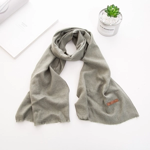 Dettaglio sciarpa in maglia verde oliva con frange e toppa in pelle su sfondo bianco