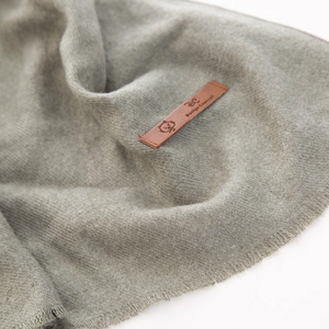 Dettaglio di sciarpa in maglia grigio-verde con toppa logo in pelle marrone premium