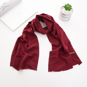 Dettaglio di una sciarpa lunga rosso scuro in finto cashmere con frange ed etichetta in cuoio