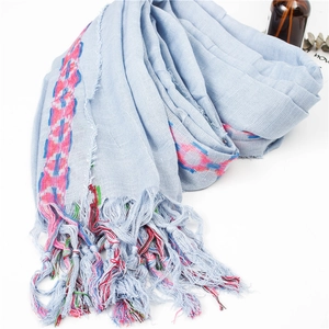 Close-up of light blue cotton linen scarf with colorful fringe tassels and woven patterns