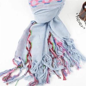 Detailed view of light blue linen scarf with colorful geometric embroidery and tassels