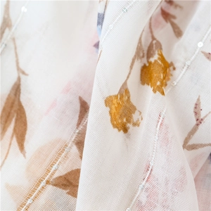 Detail of sheer cotton-linen scarf with floral print, gold ribbon, and sparkling sequins