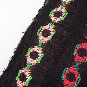 Detailed close-up of a black linen scarf featuring colorful geometric embroidery and fringe