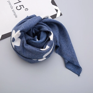 Detail of blue knit child scarf featuring white floral patterns and soft fringe edges