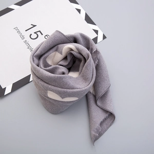 Close-up of soft knitted scarf in grey with white hearts and delicate fringe edges