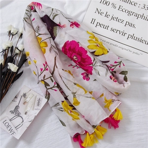 Close-up of colorful floral print shawl with pink and yellow tassels on white fabric