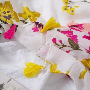 Detailed texture of white floral scarf featuring yellow blossoms and colorful tassels