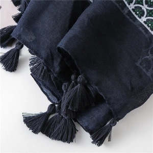 Close-up of navy scarf featuring dense tassel fringe and green embroidered geometric border
