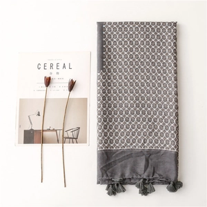 Detail of grey scarf featuring beige floral patterns and fringe edge beside a magazine